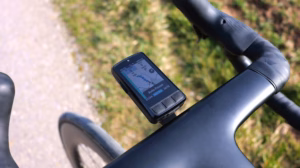 Wahoo ELEMNT BOLT bike computer on a road bike cockpit, photographed during a ride along a path beside a meadow.