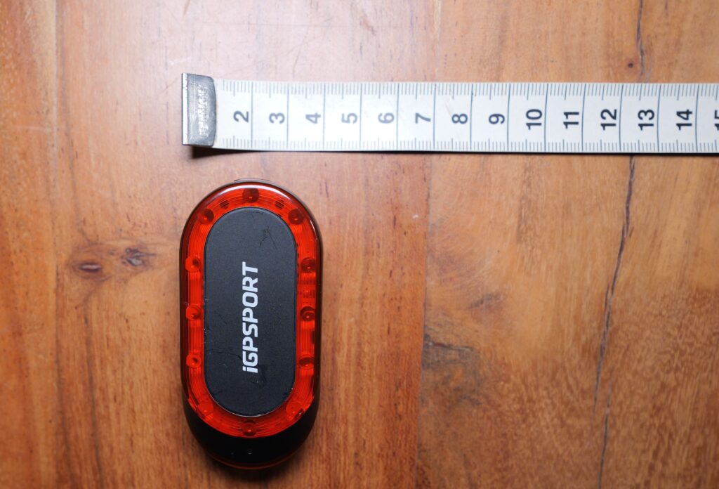 iGPSPORT SR Mini with a tape measure checking case width on a wooden table.