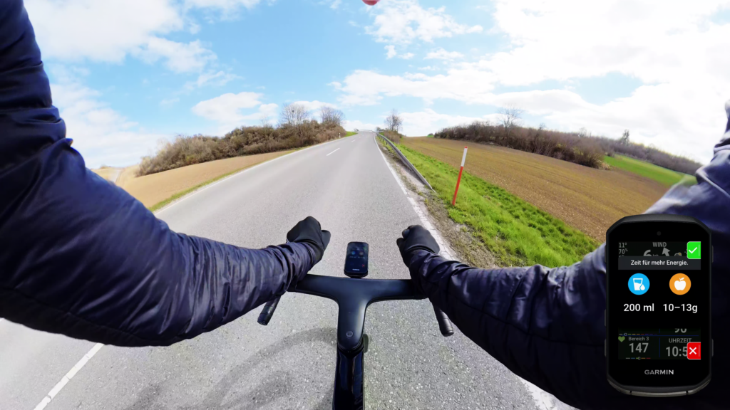 Rider's view of a country road with a bicycle handlebar and Garmin Edge 850. The display shows an energy and hydration recommendation during the ride.