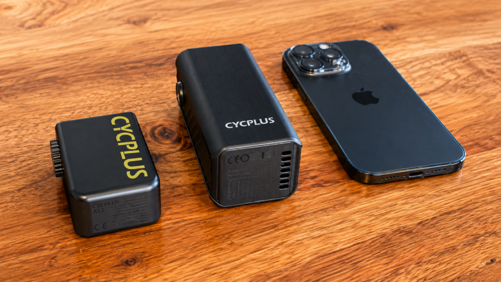 CYCPLUS A3 Mini and CYCPLUS A53 electric bike pumps compared in size beside an iPhone on a wooden table.